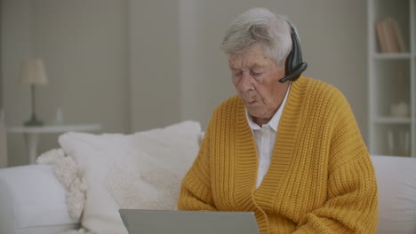 An-elderly-woman-in-her-80s-uses-a-laptop-and-headphones-for-a-video-call.-Call-to-the-hotline